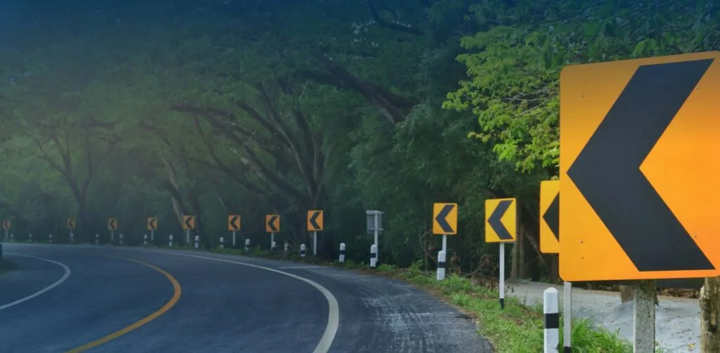 windy road with yellow left arrow signs